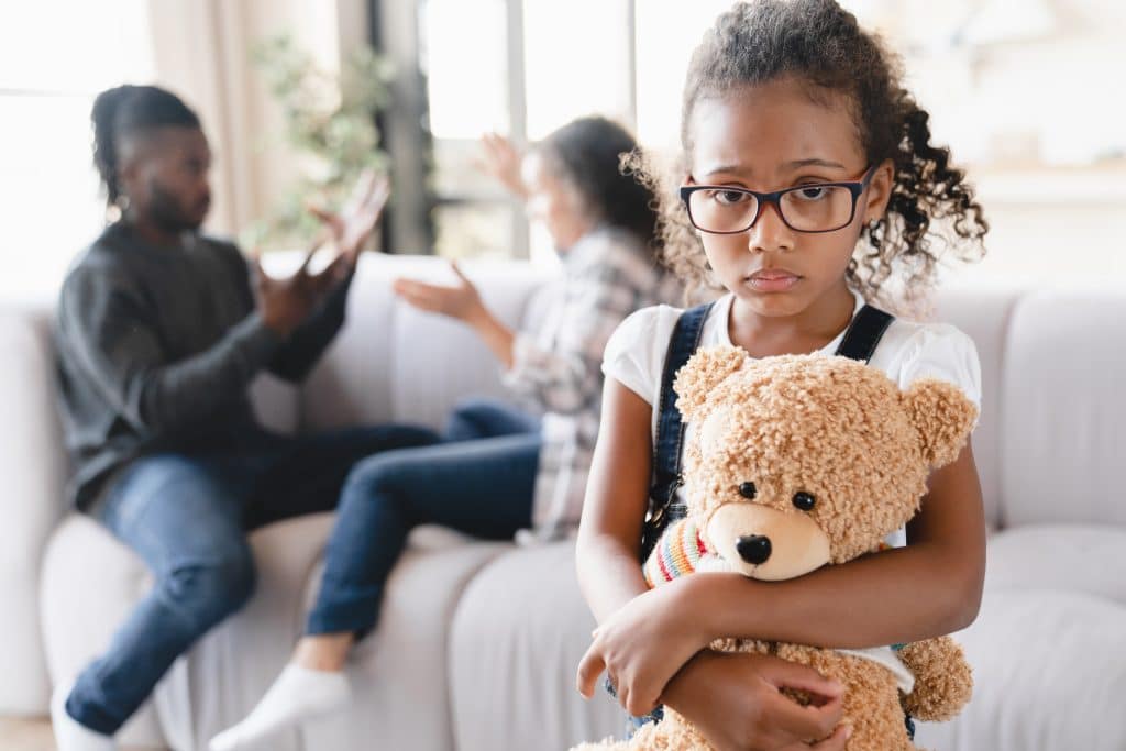 sad young girl hugging teddy bear as parents argue